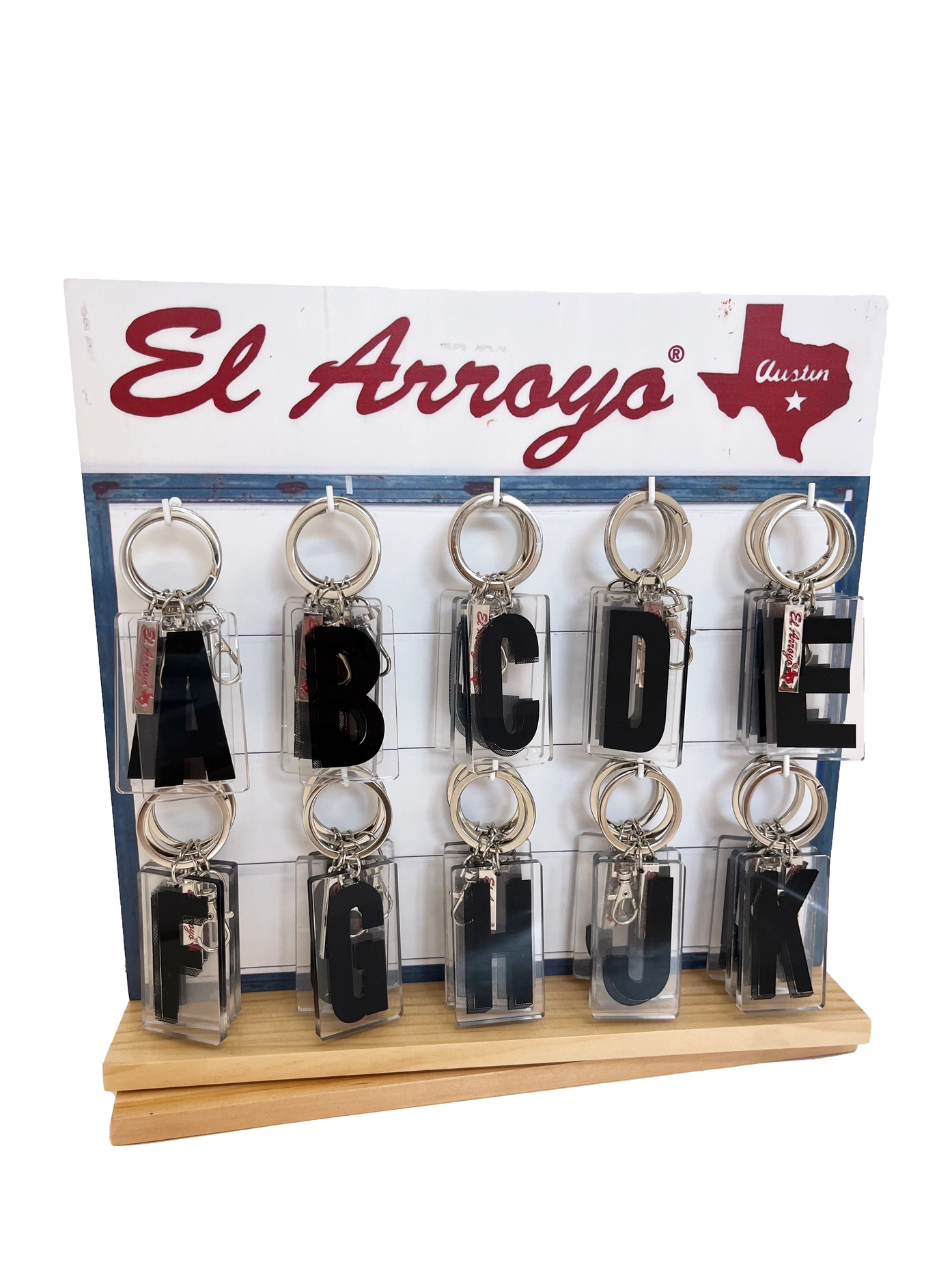 Set of keychains with letters A to L on a display stand with El Arroyo branding.
